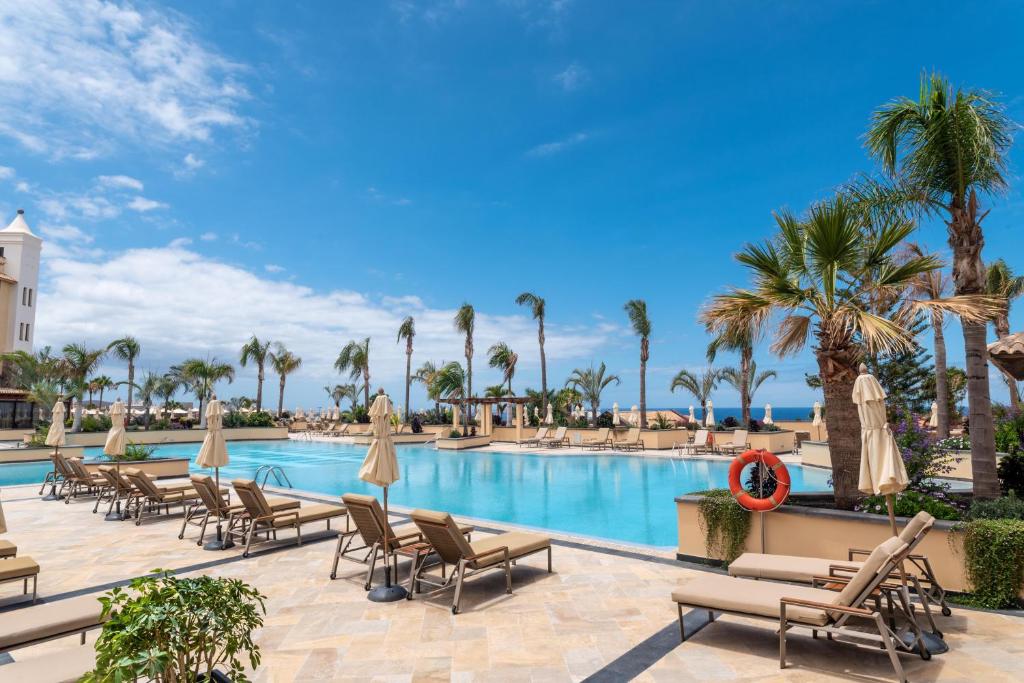 Lielisks viesnīcas baseins ar palmām un saulessargiem, kas atrodas blakus jūrai, zem skaidra debesu apgaismojuma. Ideāla vieta atpūtai un relaksācijai.