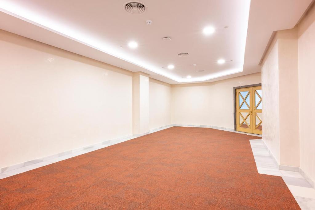 Liela un tukša telpa ar oranžu paklāju un gaišām sienām, kurā redzamas durvis ar krāsainiem stikliem. Telpa ir apgaismota ar griestu lampām.