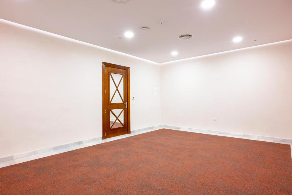 Tukša telpa ar sarkanu paklāju un koka durvīm, kas ir aprīkota ar gaismas avotiem. Ideāla vide sanāksmēm vai pasākumiem.