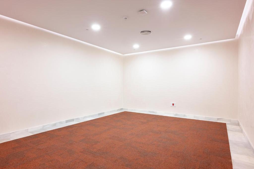 Tīra un tukša telpa ar brūnu paklāju un gaišām sienām, ideāli piemērota ofisa vai dzīvojamās zonas iekārtošanai.