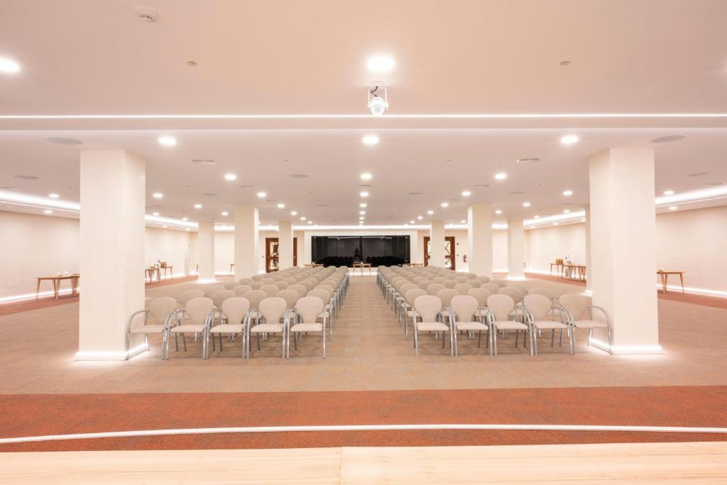 Liela konferences zāle ar rindu krēsliem un modernu apgaismojumu, sagatavota pasākumiem. Telpa ir plaša un gaiša, ar skatu uz skatuvi.