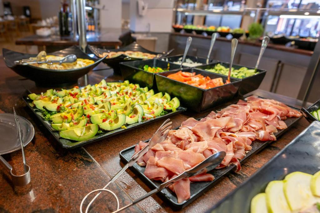 Daudzu veidu salātu un gaļas izstrādājumu bufete ar svaigiem dārzeņiem un augļiem, kas pasniegti melnās traukos.