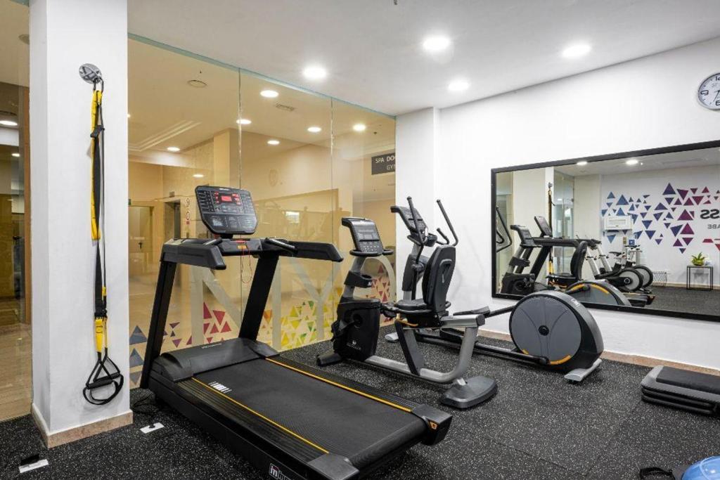 Mūsdienīgs sporta zāles iekārtojums ar skrejceliņu, trenažieriem un spoguli, nodrošinot ērtu vietu fiziskām aktivitātēm. Iekārtojums veicina veselīgu dzīvesveidu un fitnesa treniņus.