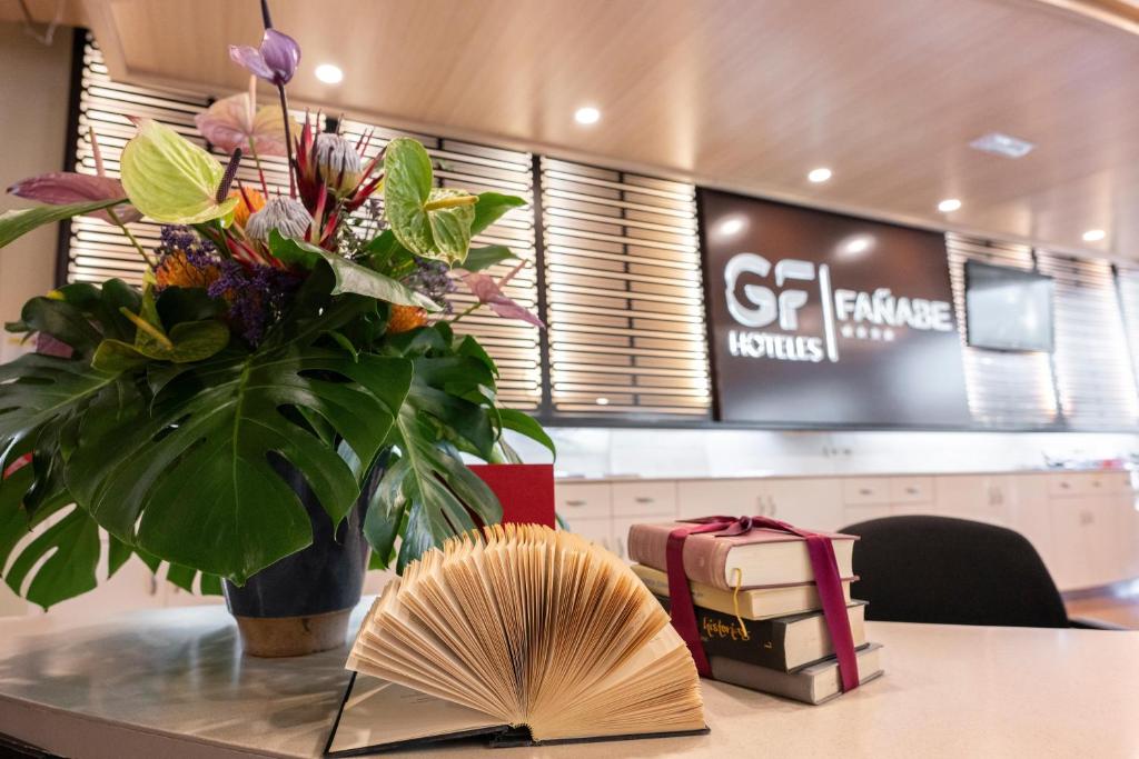 Viesnīcas reģistratūras zona ar krāšņu ziedu kompozīciju, atvērtu grāmatu un zīmolu "GF Hoteles Fañabé".