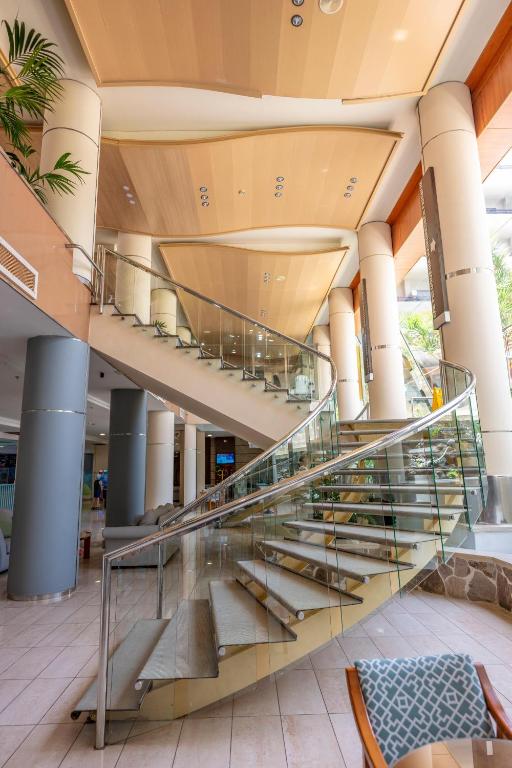 Eleganta kāpņu konstrukcija ar stikla margām un koka griestiem, kas atrodas viesnīcas vestibilā. Kāpnes veido dinamisku un modernu arhitektūras elementu.