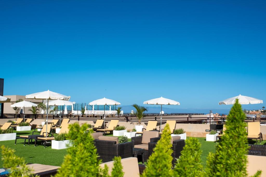 Saulaina terase ar sauļošanās krēsliem, baltiem saulessargiem un zaļo zālienu, piedāvā relaksējošu atmosfēru. Skats uz zilo debesu fona rada mierīgu un patīkamu vidi.