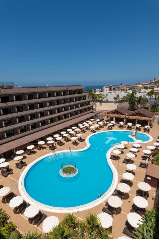 Viesnīcas baseins ar saulessargiem un atpūtas krēsliem, apkārtējo ainavu un zilo debesu fona.