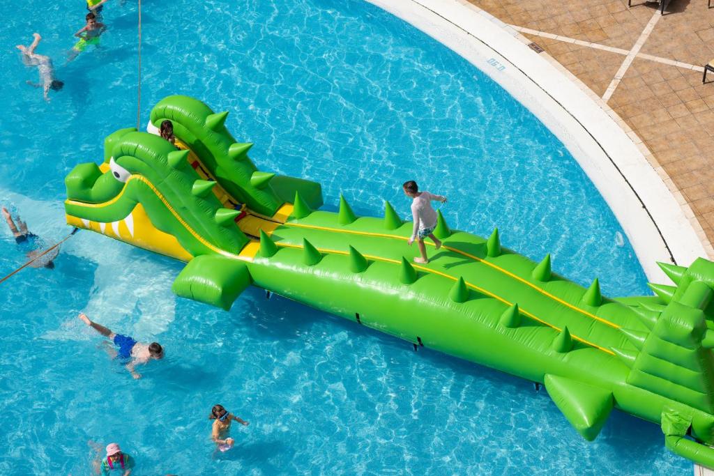 Lielais zaļais pūšamais krokodils peldbaseinā, uz kura bērni izbauda jautrus brīžus un rotaļājas.