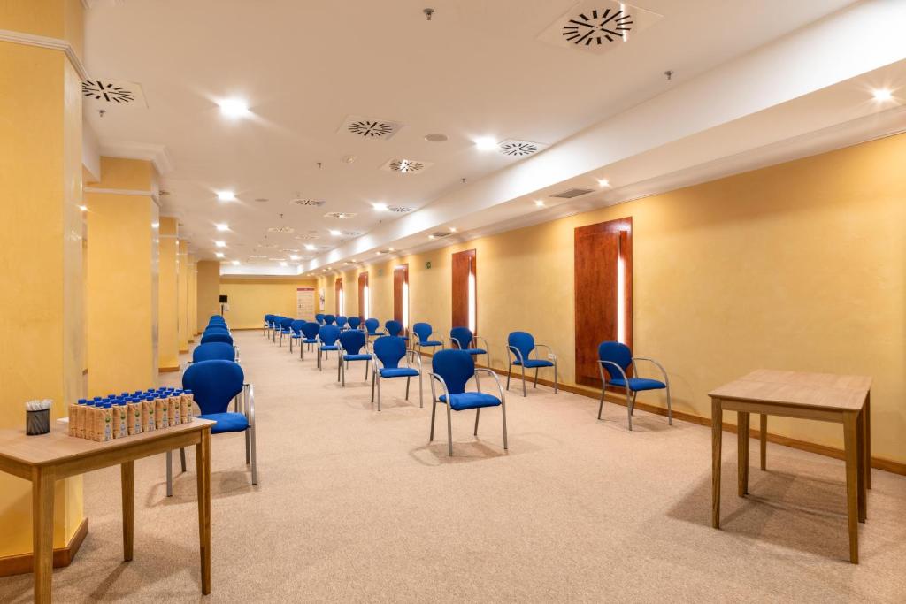 Lielas, gaišas telpas ar zilo krēslu rindu un koka galdu, kas paredzēta sanāksmēm vai pasākumiem. Telpa ir apgaismota ar dabiskiem logiem un ir mierīga atmosfēra.