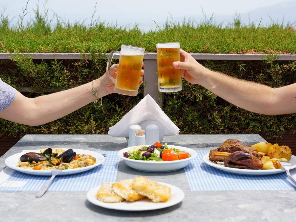Divas rokas, turēdams alus glāzes, svinīgi saskaras, kamēr uz galda ir garšīgas maltītes, tostarp jūras veltes, salāti un deserti. Gaisotne ir priecīga un apmierinoša, ideāla vasaras pusdienām.