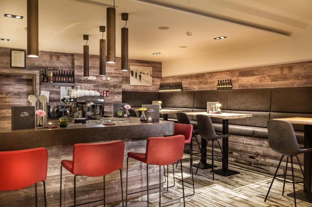 Mūsdienīgs bārs ar koka elementiem, sarkanām un pelēkām krēslām, un modernām gaismām. Interjers rada siltu un aicinošu atmosfēru, ideāli piemērots relaksācijai un sociālajiem pasākumiem.