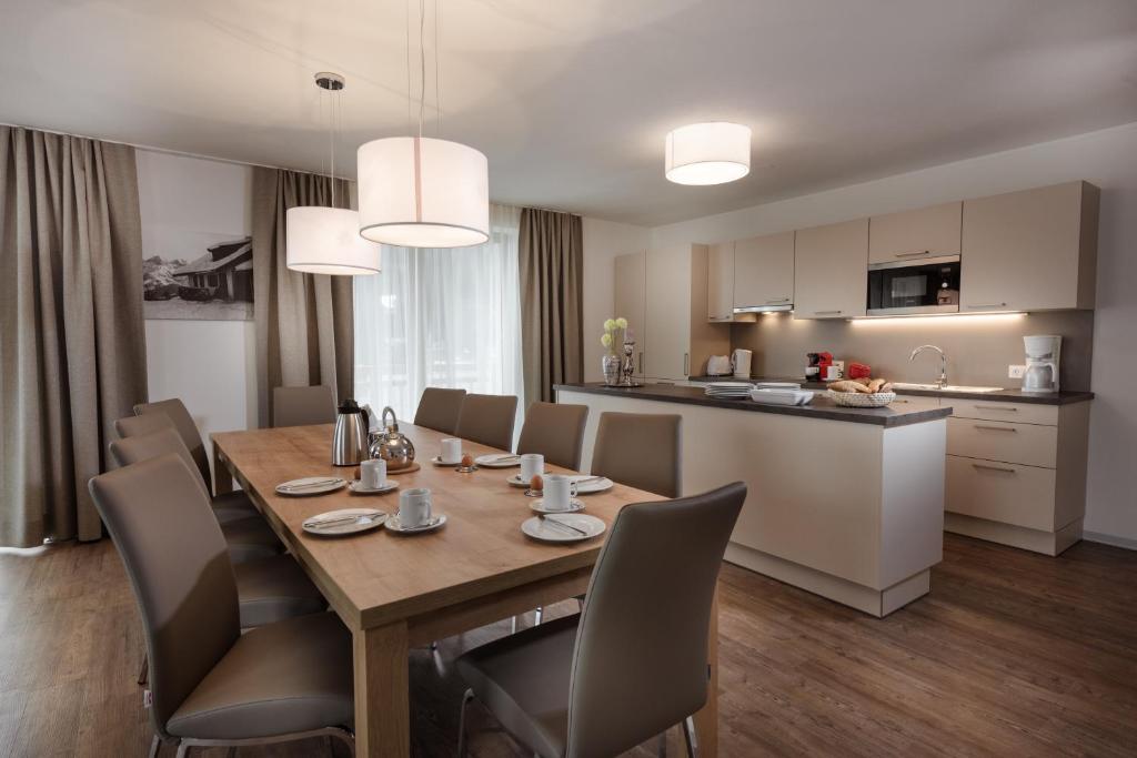 Mūsdienīga virtuve ar plašu ēdamgaldu, kas apgādāta ar galda piederumiem un ērtām krēslām. Gaismas lampas un logi rada gaišu un viesmīlīgu atmosfēru.