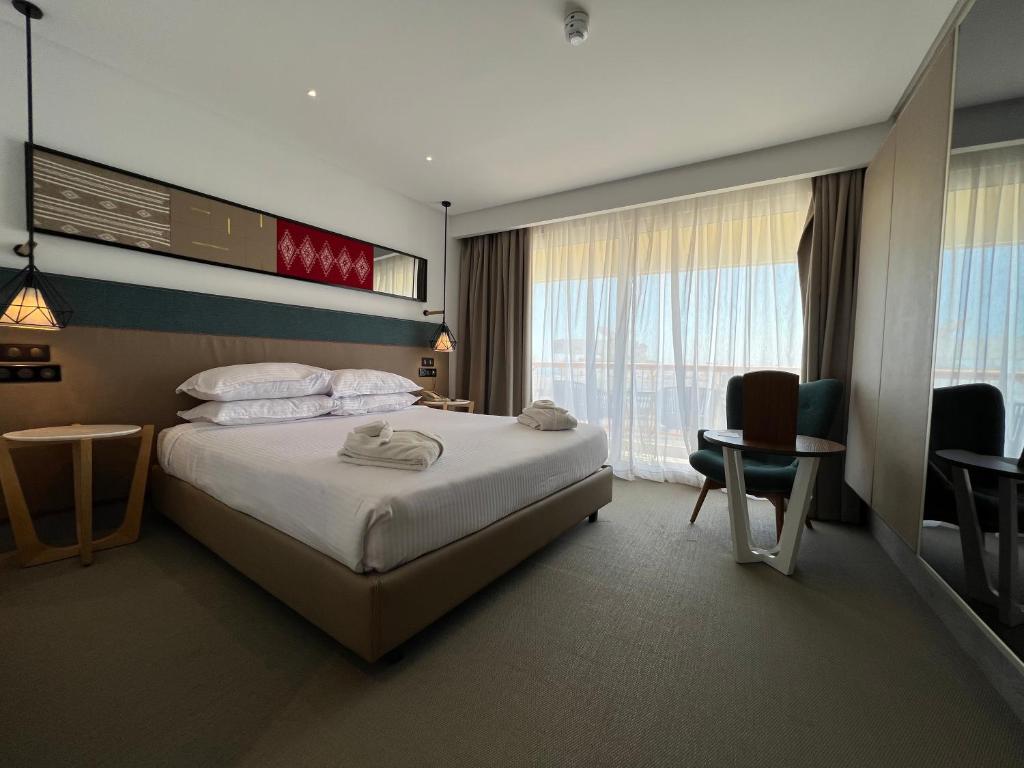 Mūsdienīgs viesnīcas numurs ar divguļamo gultu, mīkstiem spilveniem un skatu uz terasi. Interjerā ir stilīgas lampas un moderns mēbeļu dizains.