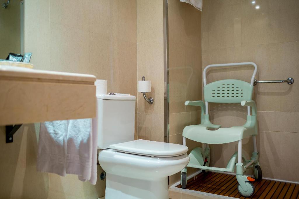 Mūsdienīgs vannas istabas interjers ar tualeti, dušas zonu un īpaši pielāgotu krēslu. Sienas apdare ir gaiša, radot tīras un ērtas atmosfēras sajūtu.