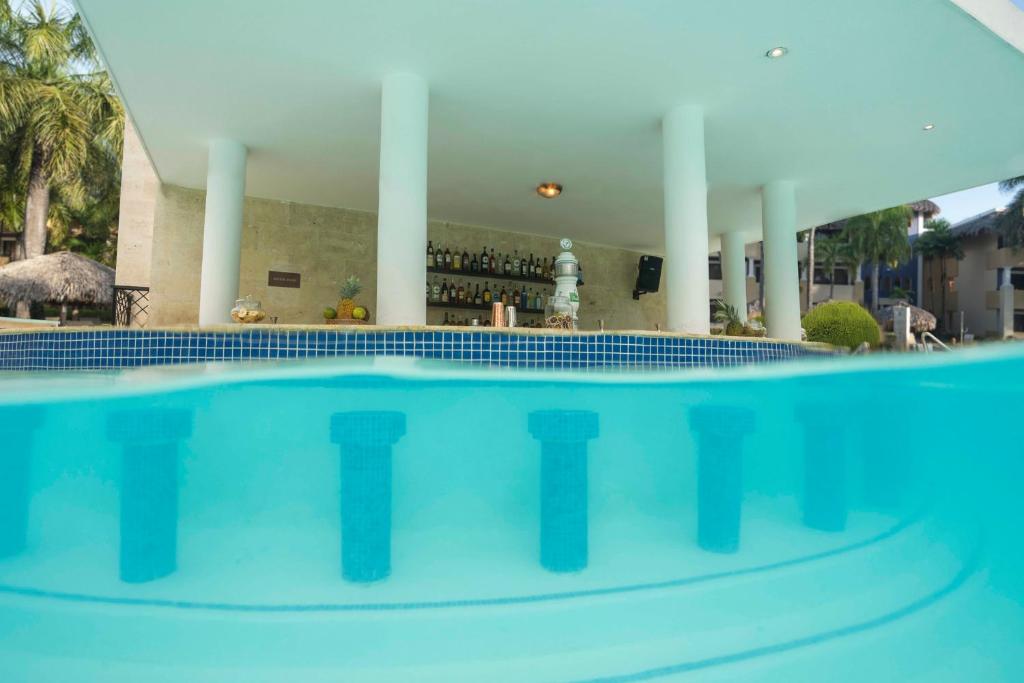 Baseins ar bāru, kas atrodas zem jumta, redzams caur ūdeni. Apkārtējos kokos un zaļumos ir atpūtas zona.