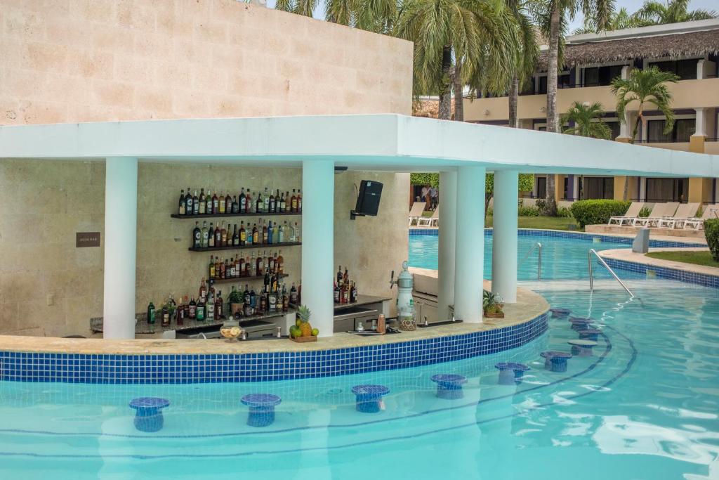 Baseins ar bāru, kurā redzami dažādi dzērieni un kokteiļi, atrodas pie ūdens. Apkārt ir palmām ieskauts viesnīcas komplekss un atpūtas zonas.