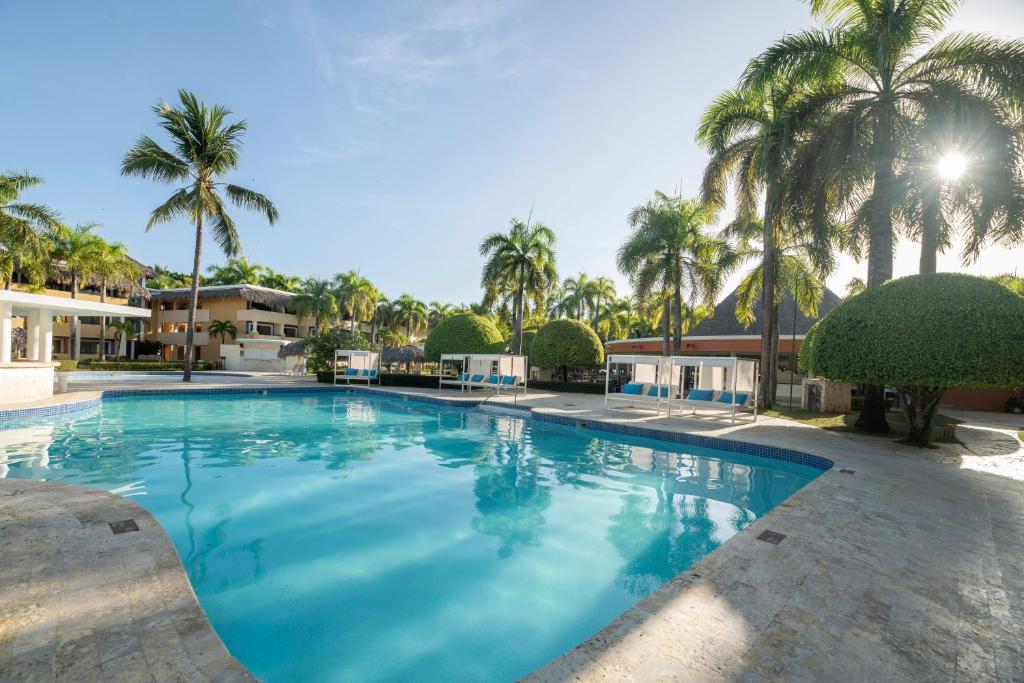 Labi uzturēts baseins ar palmām un viesnīcu fonā, saulaina diena. Ideāla vieta relaksācijai un atpūtai.