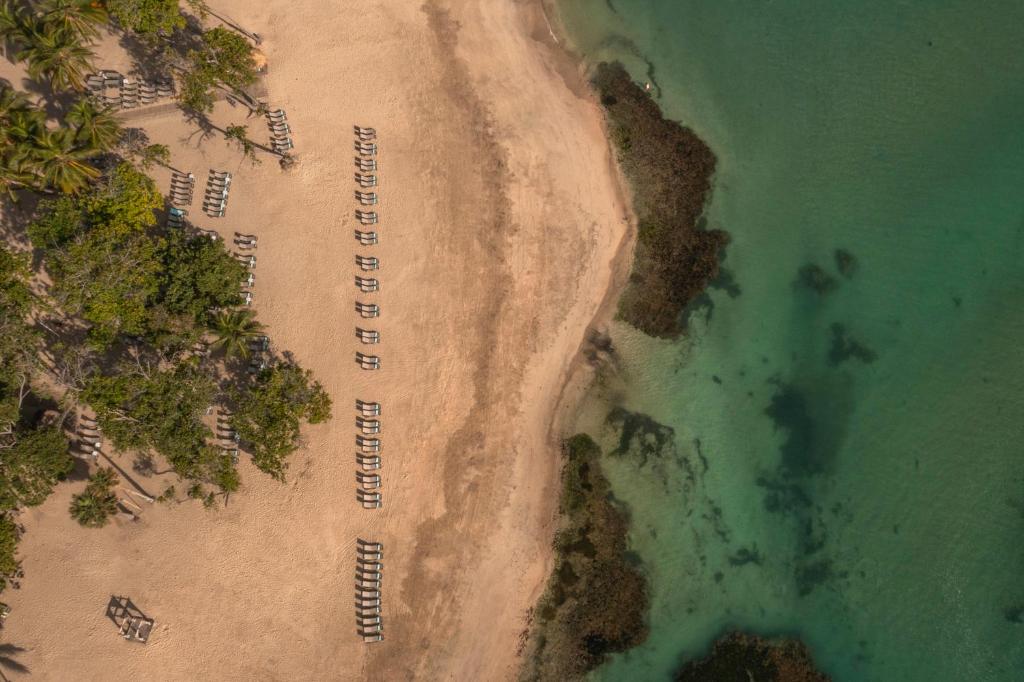 Pludmale ar saulessargiem un palmām, redzama no augšas. Kristāldzidrs ūdens un smilšaina krasta līnija veido mierīgu atpūtas vietu.