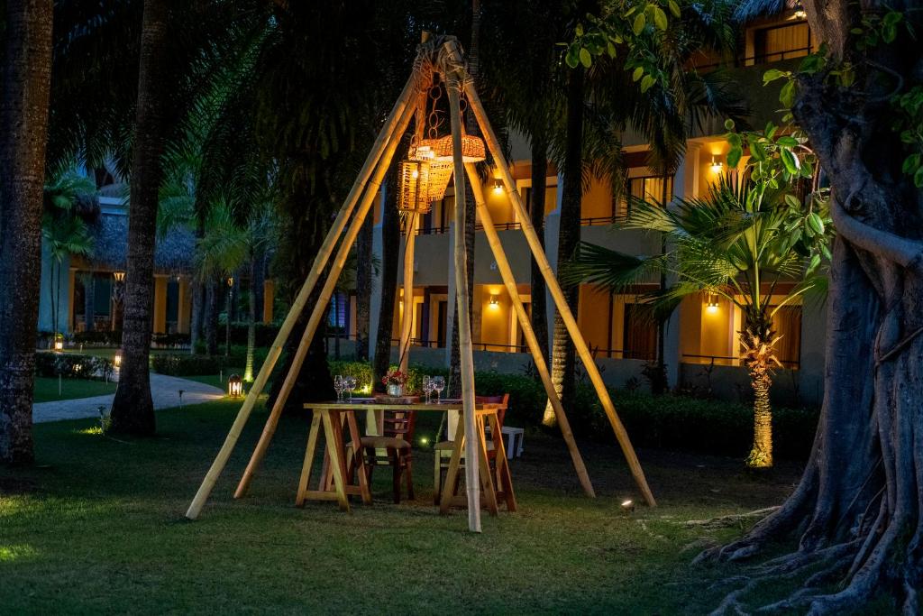 Dārza svinību vieta ar koka konstrukciju un apgaismojumu, kas radīts romantiskai atmosfērai. Apkārt palmām un viesnīcas ēkai ir redzami gaismas avoti.