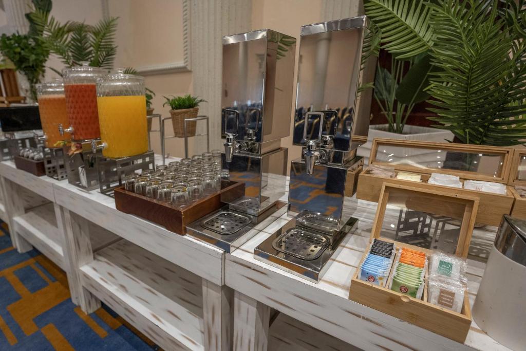 Dzerienu stacija ar dažādām sulām un tējas maisiņiem, izvietota uz eleganta galda ar ziediem un lapām.