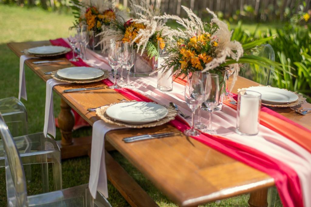 Elegants galda klājums ar ziedu kompozīcijām, stikla traukiem un dekoratīvām salvetēm, kas rada svinīgu atmosfēru dabā. Ideāli piemērots pasākumiem vai svinībām.