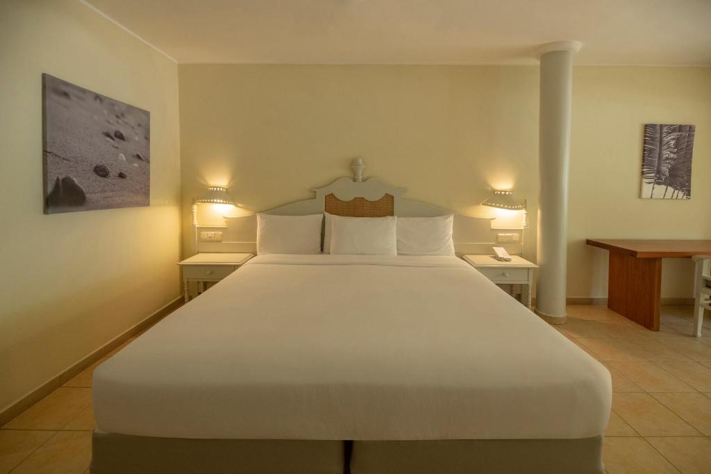 Mūsdienīga viesnīcas numura iekārtojums ar plašu gultu, blakus naktsgaldiņiem un mājīgu darba galdu. Sienas rotā mākslas darbi, radot relaksējošu atmosfēru.