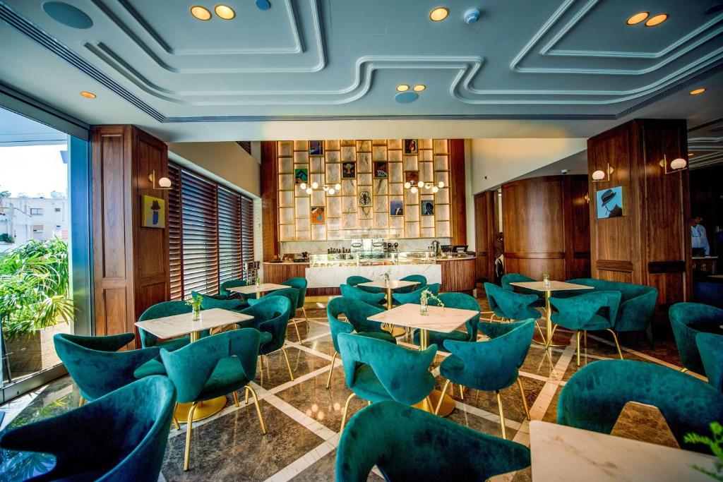 Mūsdienīga kafijas veikala iekārtojums ar elegantiem zaļiem krēsliem un marmora galdiem. Interjerā ir koka elementi un mākslinieciskas dekorācijas, radot patīkamu atmosfēru.