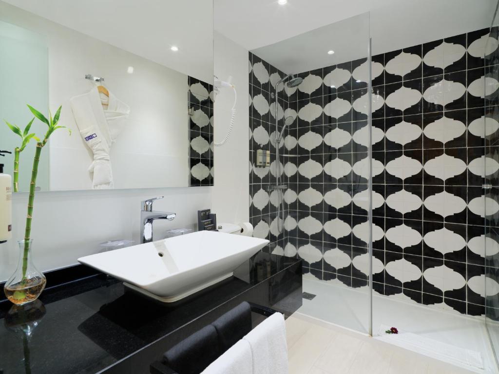 Mūsdienīgs vannas istabas interjers ar elegantiem melnbaltiem flīzēm, minimālistisku izlietni un augu dekoru. Vannas istabā ir stikla duša un mīksts dvielis, kas piešķir mājīgumu.