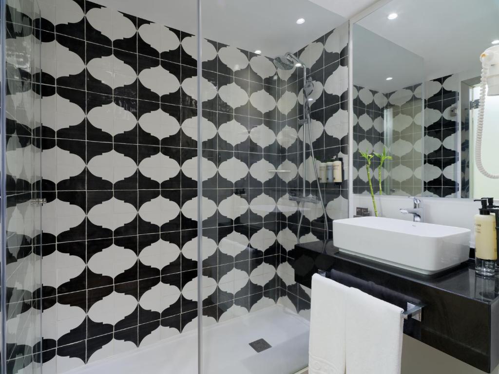 Mūsdienīgs vannas istabas interjers ar melnu un baltu flīžu rakstu, modernu izlietni un spoguļiem, radot elegantu atmosfēru.