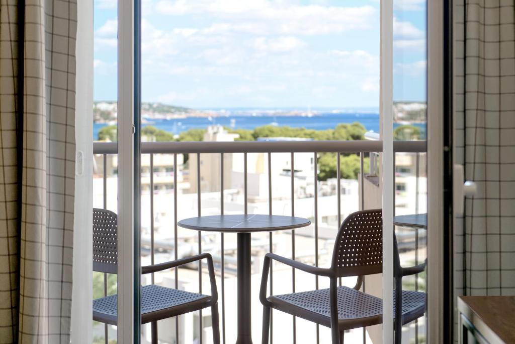 Skats no viesnīcas balkona uz jūru, kur divi krēsli un galds aicina uz atpūtu. Jūra un apkārtējā ainava veido mierīgu atmosfēru.