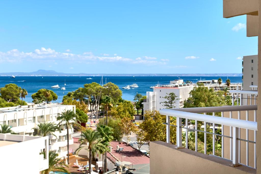 Skats uz jūru ar jahtām un pludmales ainavu, skaidrā debesīs un zaļiem kokiem. Ideāls skats uz atpūtu pie ūdens.