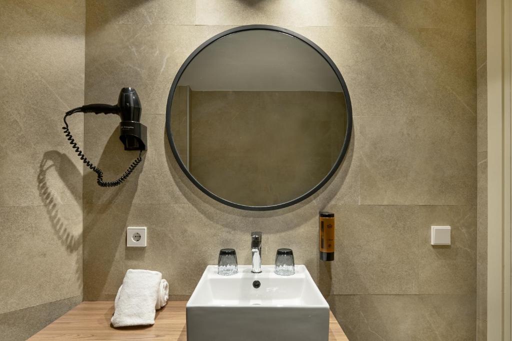 Mūsdienīgs vannas istabas dizains ar apaļu spoguļu un matu fēnu, kas piestiprināts pie sienas, un elegantu izlietni. Sienas apdare ir vienkārša un stilīga, radot patīkamu atmosfēru.