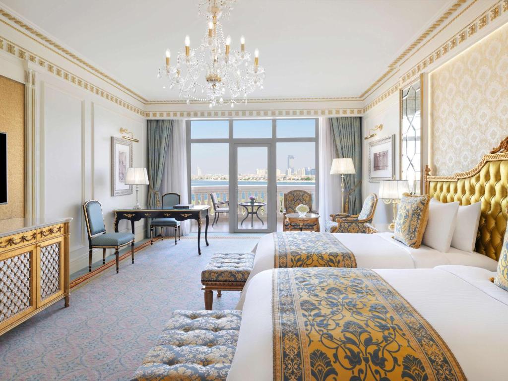 Elegants viesnīcas numurs ar divām gultām, zeltu rotātiem aksesuāriem un skatu uz pilsētu caur lieliem logiem. Numurā ir arī rakstāmgalds un atpūtas zona.