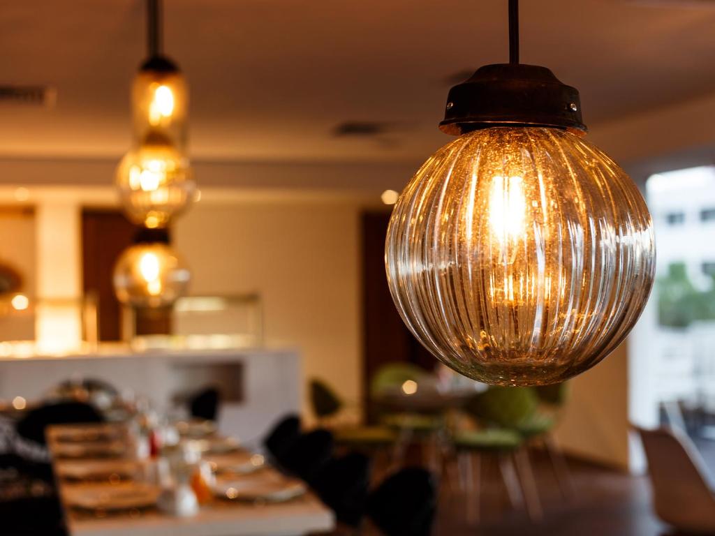 Stilīga apgaismojuma lampa ar caurspīdīgu, svītrainu dizainu, kas radījusies modernā restorāna interjerā. Siltā gaisma piešķir mājīgumu un atmosfēru.