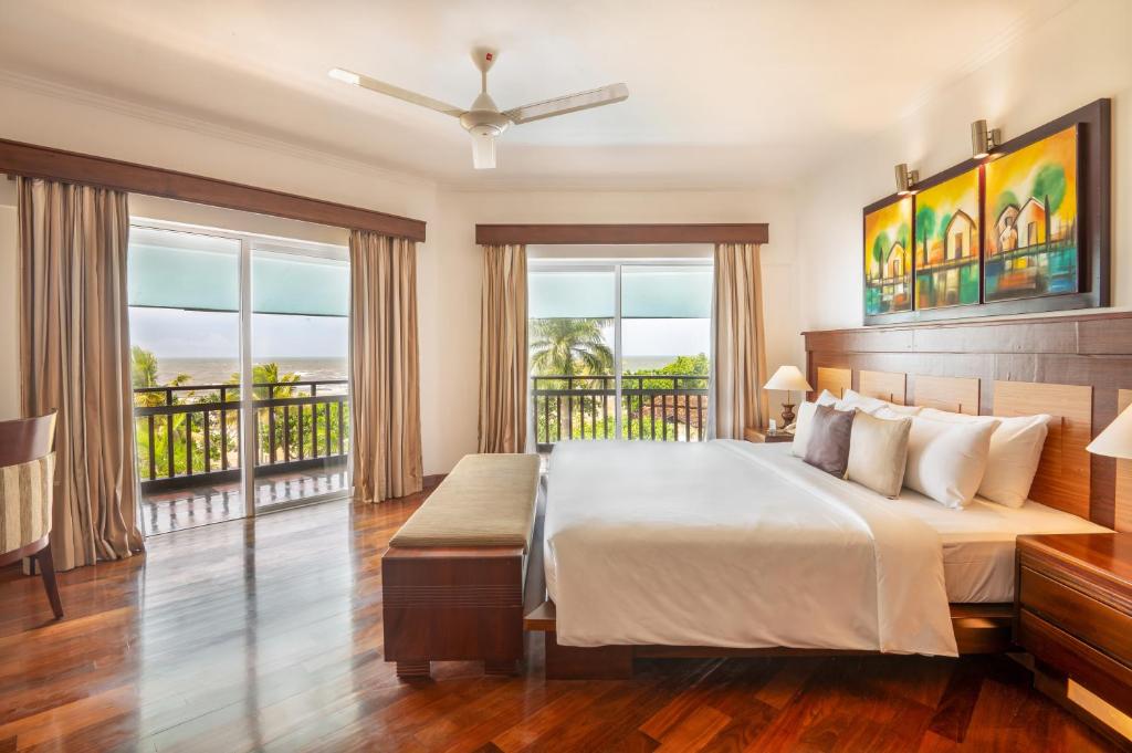 Mūsdienīga guļamistaba ar plašu logu, no kura paveras skats uz dārzu un jūru. Interjerā ir koka grīdas, gaismas toņu gultas veļa un mākslas darbi uz sienām.