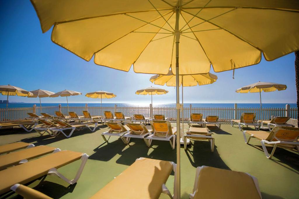 Saulainā pludmales atpūtas zona ar dzelteniem lietussargiem un sauļošanās krēsliem, skats uz jūru un skaidru debesi. Ideāla vieta relaksācijai un saules baudīšanai.