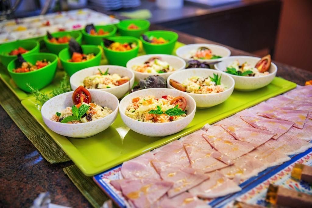 Svaigu salātu un ēdienu izkārtojums ar zaļām bļodām, kas piepildītas ar dažādiem dārzeņiem un graudiem, līdzās plakanētiem gaļas šķēlītēm.