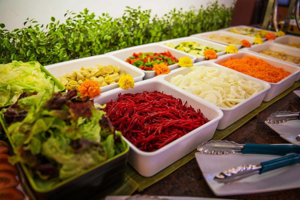 Dārzeņu bufete ar dažādu veidu salātiem un garnējumiem, tostarp sarkaniem pipariem, burkāniem un sīpoliem. Krāsaini dārzeņi un svaigas zaļumi veido pievilcīgu un veselīgu ēdienu izvēli.