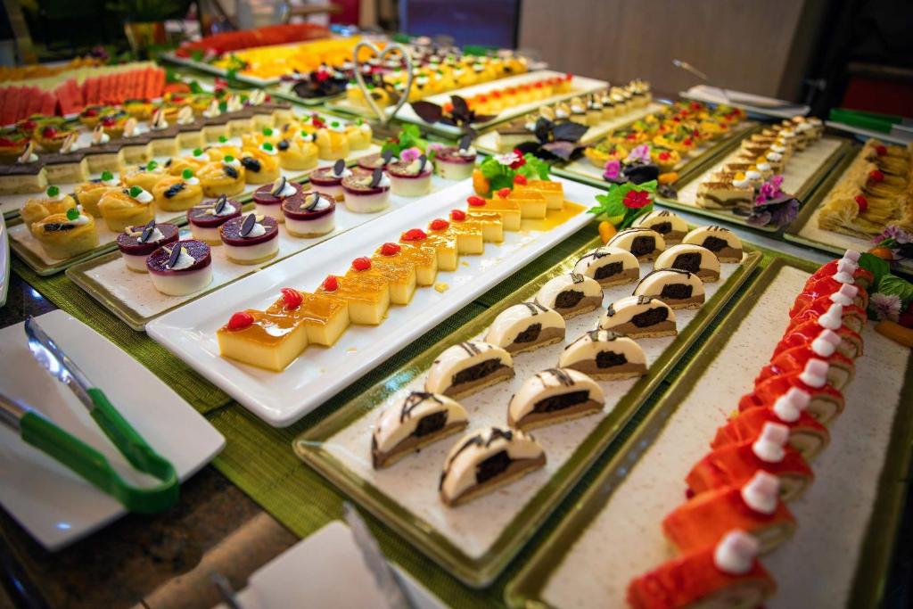 Saldumu bufete ar dažādiem desertiem, tostarp krēmīgām kūkām, augļu želejām un rotājumiem ar ziediem. Krāsainie un izsmalcinātie saldumi ir izlikti uz elegantām šķīvjiem.