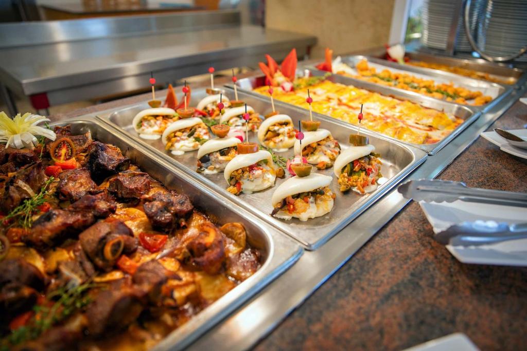 Bagātīgs bufetes galds ar dažādiem ēdieniem, tostarp gaļas un dārzeņu ēdieniem, kā arī dekoratīviem uzkodu šķīvjiem. Ideāli piemērots svinībām un svinīgām maltītēm.