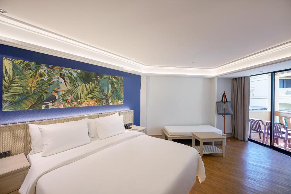 Moderns viesnīcas numurs ar plašu gultu un krāsainu tropu mākslas darbu uz sienas. Numurā ir liels logs ar piekļuvi terasei un minimālistisks dizains.