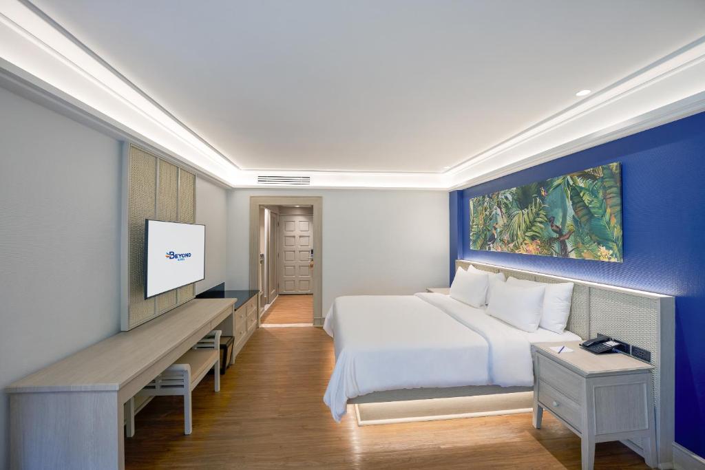 Moderns viesnīcas numurs ar plašu gultu, TV un stilīgu apgaismojumu. Uz sienas redzams krāsains augu motīvs, radot relaksējošu atmosfēru.