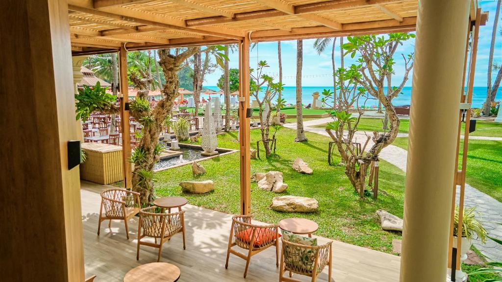 Terase ar skatu uz jūru, kur ir rattan krēsli un galdi, apkārt ir zaļš zālājs un palmas. Šī vieta ir ideāla relaksācijai un baudīšanai.