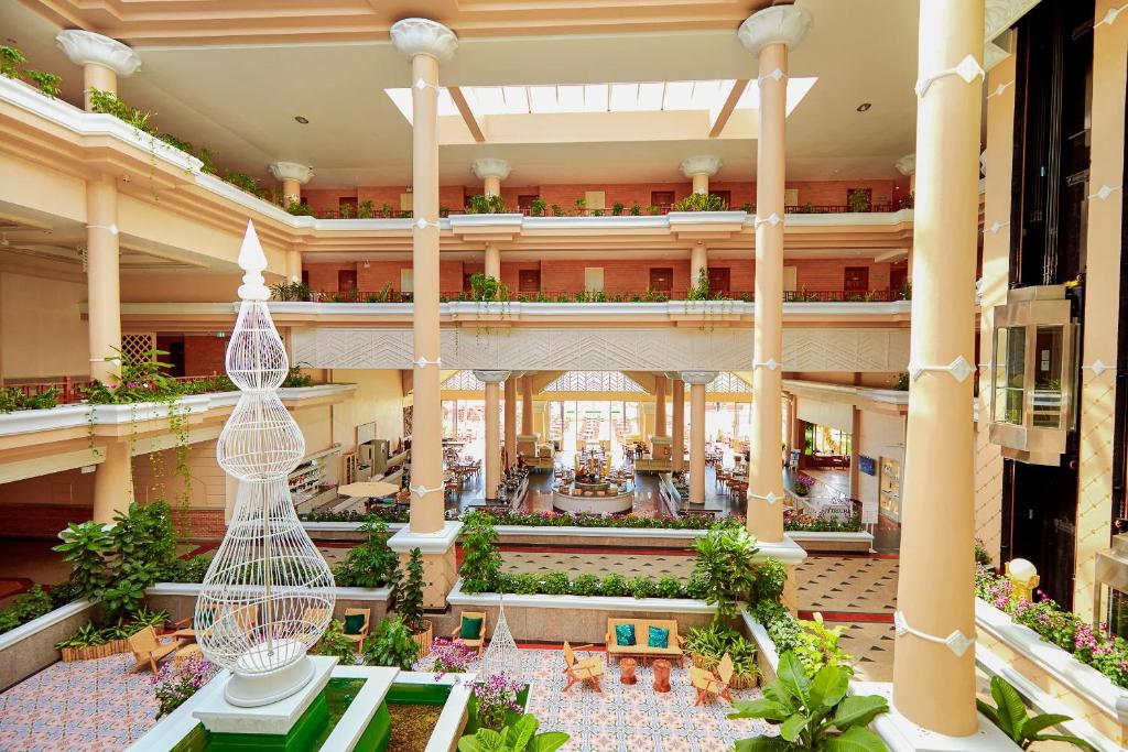 Lielisks viesnīcas interjers ar modernu arhitektūru, kas ietver plašas telpas, zaļas augu dekorācijas un centrālo strūklaku. Gaismas plūsma no augšējiem logiem rada patīkamu atmosfēru.