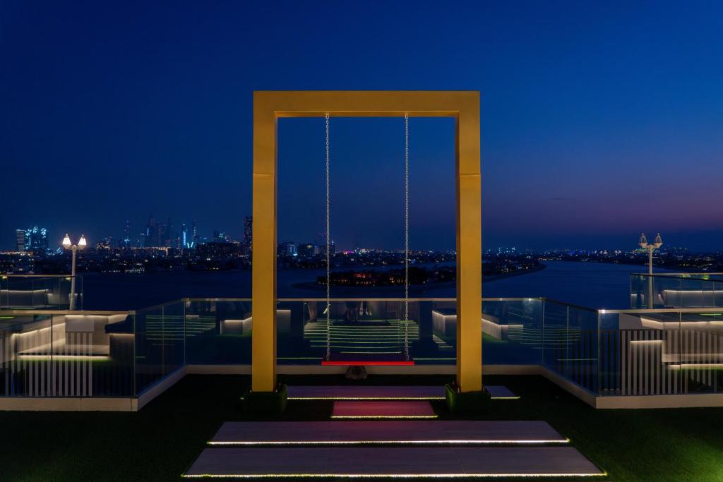 Rooftop swing set against a stunning city skyline at dusk, illuminated by soft lights. The scene captures a blend of urban elegance and tranquility.
