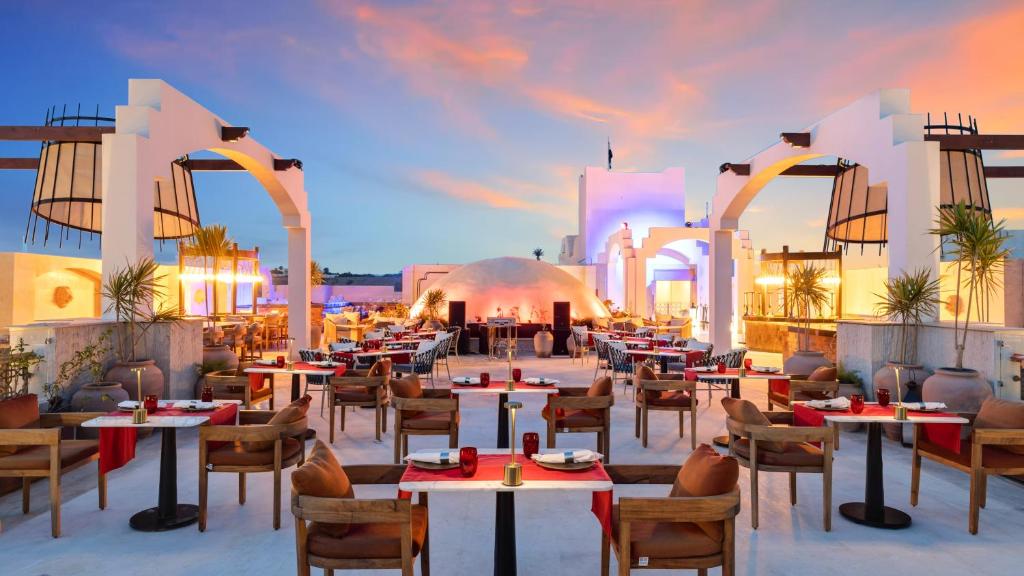 Elegantā terase ar modernu interjeru un skaistu saulrietu, kurā ir galdi un krēsli, aicina apmeklētājus baudīt maltītes un relaksējošu atmosfēru.