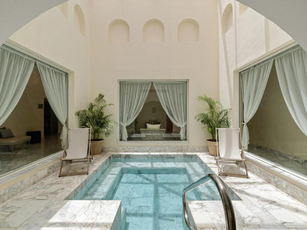 Mūsdienīga iekštelpu peldvieta ar marmora grīdu un lieliem logiem, kas nodrošina dabisko apgaismojumu. Telpā ir ērtas atpūtas krēsli un zaļās iekārtojuma augu akcenti.