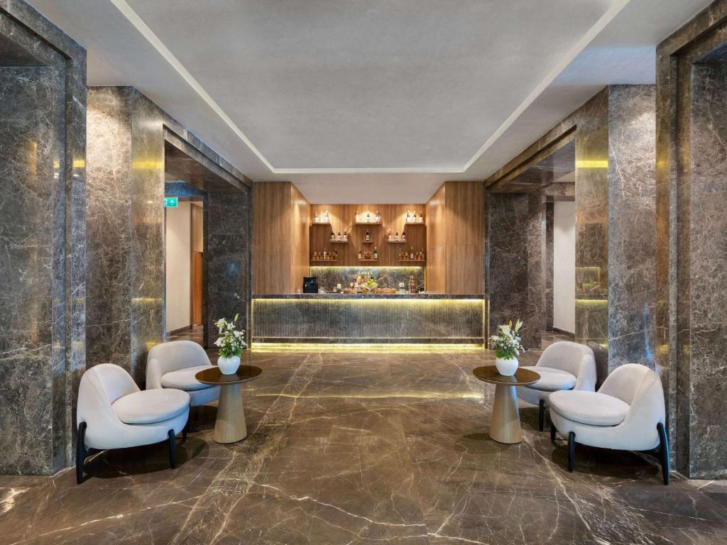 Mūsdienīgs viesnīcas reģistratūras interjers ar marmora grīdu un elegantām baltām krēslām, kas papildinātas ar koka akcentiem un ziedu kompozīciju.