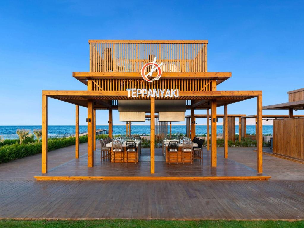 Koka terase ar atvērtu telpu un ēdamgaldu, kas atrodas pie jūras, ar lielu zīmi 