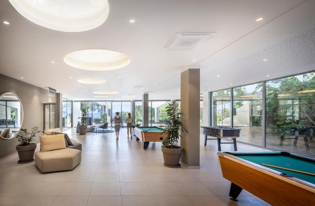 Mūsdienīga atpūtas telpa ar biljarda galdu un galda futbolu, gaiša un plaša, ar lieliem logiem, kas sniedz skatu uz dārzu.